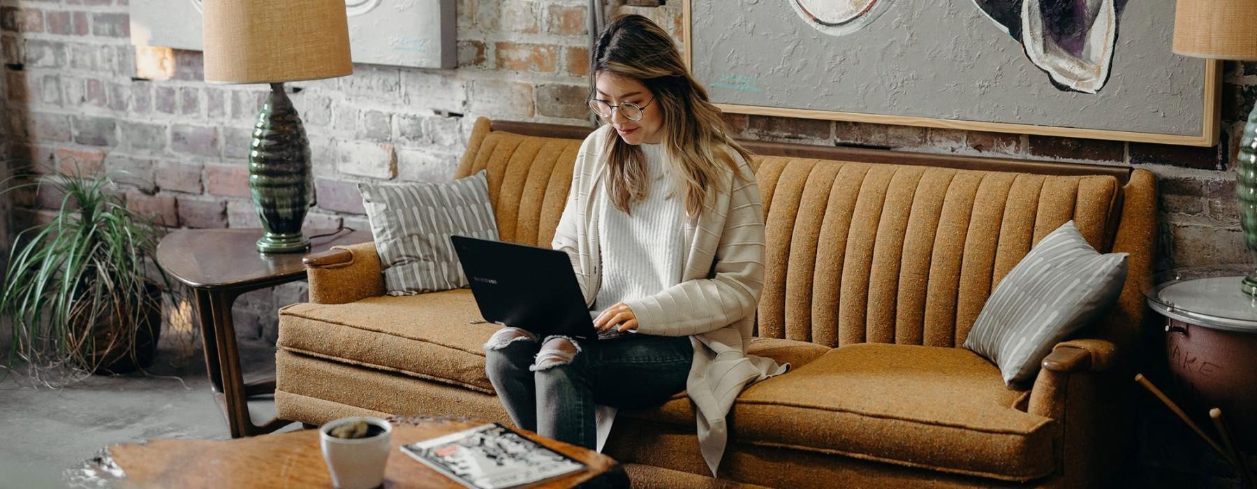 a woman sitting on a couch working on a laptop